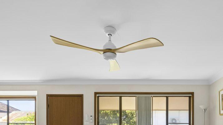 Ventilador de techo de diseño moderno con aspas de madera instalado en un salón luminoso, preparado para usar su función de invierno