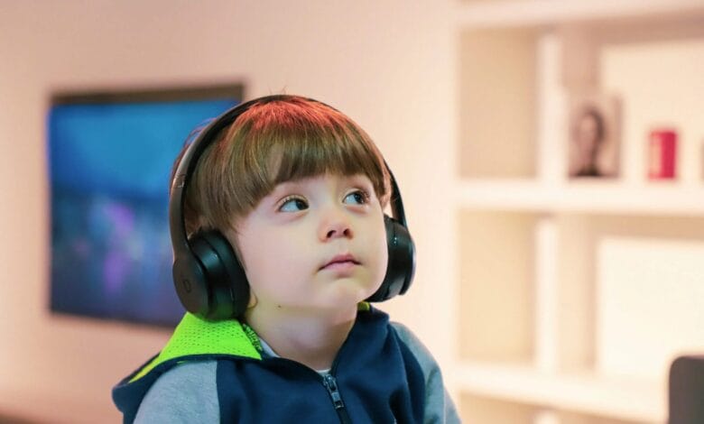 Niño pequeño usando una tableta con una sonrisa, mientras un padre o madre supervisa de fondo.