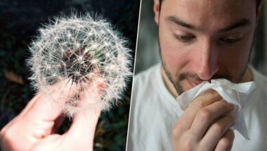 Persona con mascarilla cubriendo su boca y nariz en un entorno al aire libre con flores y árboles en flor