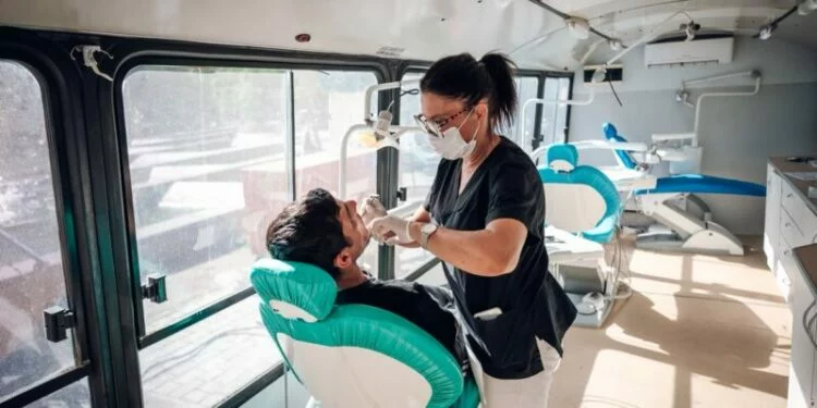 Persona sonriendo saludablemente, con un odontólogo realizando un chequeo bucal en el fondo
