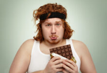Hombre oliendo una barra de chocolate antes de hacer extensiones de piernas en el gimnasio