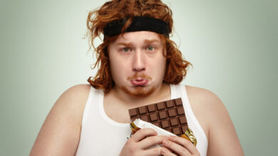 Hombre oliendo una barra de chocolate antes de hacer extensiones de piernas en el gimnasio
