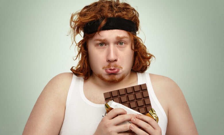 Hombre oliendo una barra de chocolate antes de hacer extensiones de piernas en el gimnasio