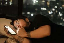 Persona acostada en la cama deslizando el móvil bajo la luz tenue